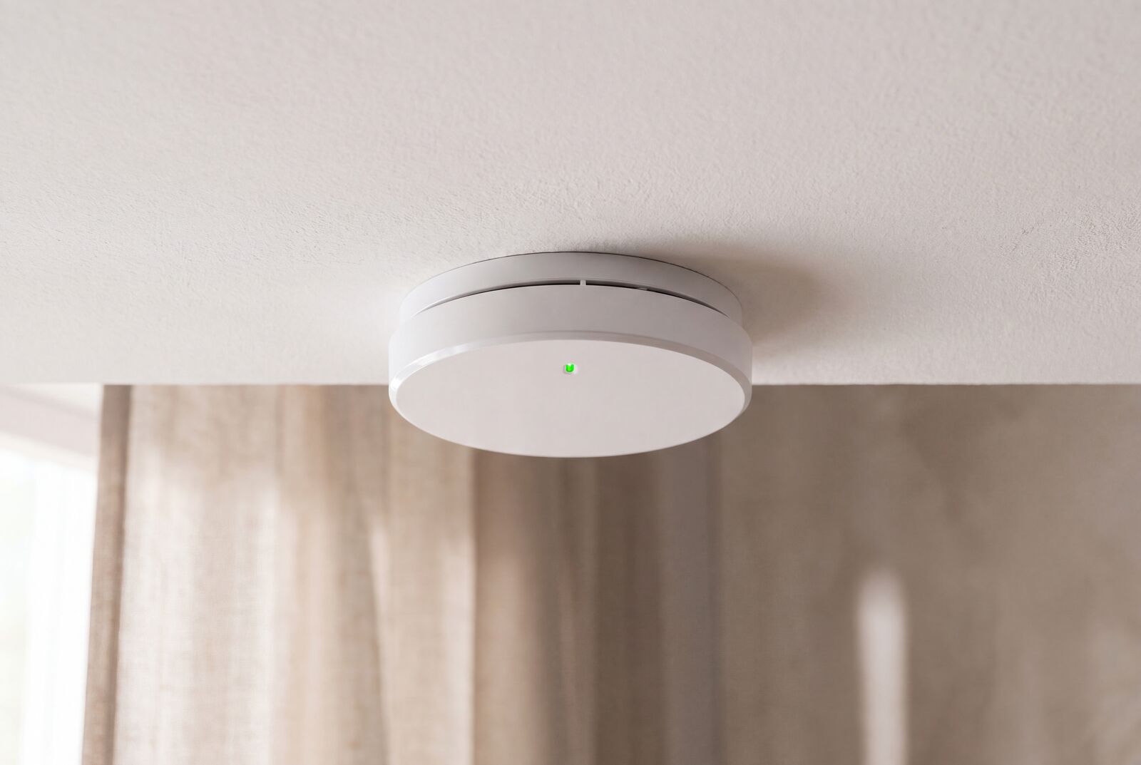 Product still: a round smoke alarm with a green indicator on linen